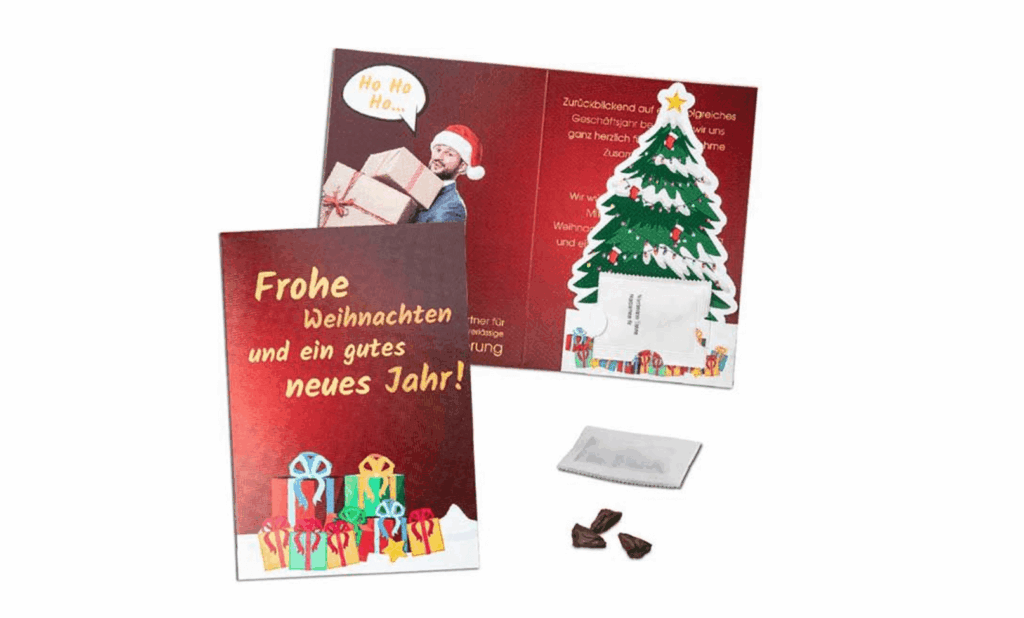 Eine bedruckte Weihnachtskarte ist aufgeklappt. Auf der roten Weihnachtskarte ist ein grüner Tannenbaum zu sehen. Des Weiteren ein Mann mit einer roten Weihnachtsmannmütze.